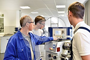 Young apprentices in technical vocational training are taught by older trainers on a cnc lathes machine