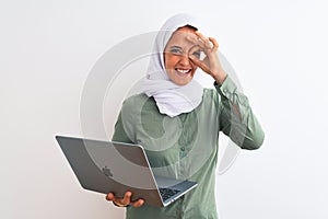 Young Arab business woman wearing hijab using laptop over isolated background with happy face smiling doing ok sign with hand on