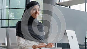 Young arab businesswoman in hijab working on computer smiling enjoying office work successful woman professional manager