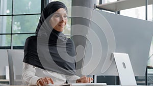 Young arab businesswoman in hijab working on computer smiling enjoying office work successful woman professional manager