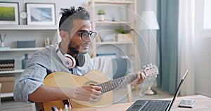 Young Arab guitarist playing the guitar and using laptop at home alone