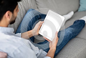 Young arab guy holding digital tablet with blank white screen, showing new app or browsing website, mockup for design