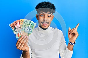 Young arab handsome man holding australian dollars smiling happy pointing with hand and finger to the side