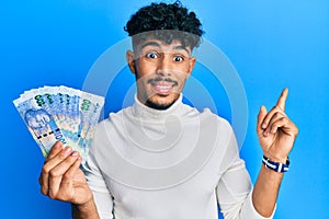Young arab handsome man holding south african 100 rand banknotes smiling happy pointing with hand and finger to the side