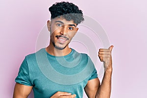 Young arab handsome man wearing casual clothes smiling with happy face looking and pointing to the side with thumb up