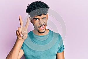 Young arab handsome man wearing casual clothes smiling with happy face winking at the camera doing victory sign