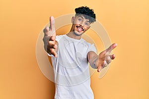 Young arab handsome man wearing casual white tshirt looking at the camera smiling with open arms for hug