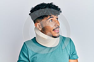 Young arab handsome man wearing cervical neck collar looking away to side with smile on face, natural expression