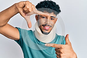 Young arab handsome man wearing cervical neck collar smiling making frame with hands and fingers with happy face