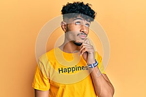 Young arab handsome man wearing tshirt with happiness word message thinking concentrated about doubt with finger on chin and