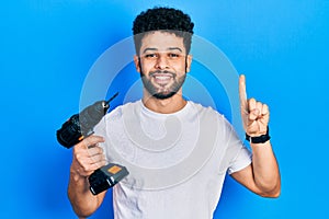 Young arab man with beard using drill smiling with an idea or question pointing finger with happy face, number one