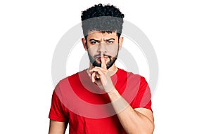 Young arab man with beard wearing casual red t shirt asking to be quiet with finger on lips