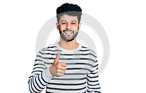 Young arab man with beard wearing casual striped sweater doing happy thumbs up gesture with hand