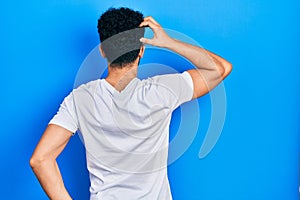 Young arab man with beard wearing casual white t shirt backwards thinking about doubt with hand on head