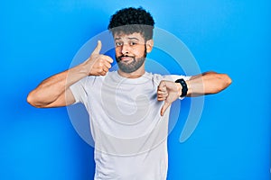 Young arab man with beard wearing casual white t shirt doing thumbs up and down, disagreement and agreement expression