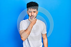 Young arab man with beard wearing casual white t shirt looking fascinated with disbelief, surprise and amazed expression with