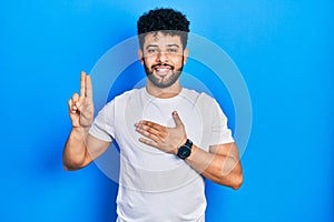 Young arab man with beard wearing casual white t shirt smiling swearing with hand on chest and fingers up, making a loyalty