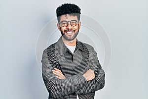 Young arab man with beard wearing glasses with arms crossed gesture smiling and laughing hard out loud because funny crazy joke