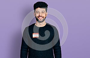 Young arab man with beard wearing hello my name is sticker identification looking positive and happy standing and smiling with a