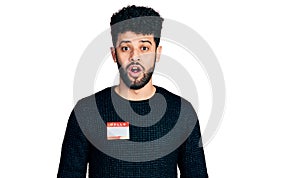 Young arab man with beard wearing hello my name is sticker identification scared and amazed with open mouth for surprise,
