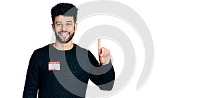 Young arab man with beard wearing hello my name is sticker identification smiling with an idea or question pointing finger with