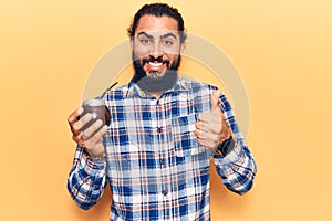 Young arab man drinking mate infusion smiling happy and positive, thumb up doing excellent and approval sign