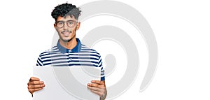 Young arab man holding blank empty banner looking positive and happy standing and smiling with a confident smile showing teeth