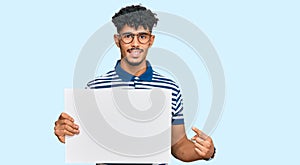 Young arab man holding blank empty banner smiling happy pointing with hand and finger