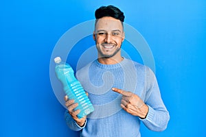 Young arab man holding detergent bottle smiling happy pointing with hand and finger