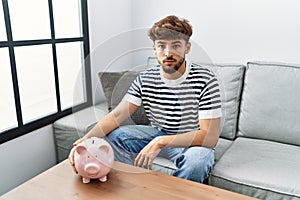 Young arab man holding piggy bank thinking attitude and sober expression looking self confident