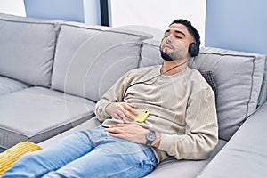 Young arab man listening to music sleeping on sofa at home