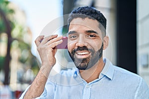 Young arab man miling confident listening audio message by the smartphone at street