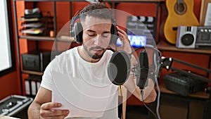 Young arab man musician wearing headphones singing song at music studio