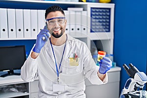 Young arab man scientist talking on the smartphone holding urine test tube analysis at laboratory
