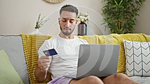 Young arab man shopping with laptop and credit card sitting on sofa at home