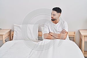 Young arab man sitting on bed with angry expression and arms crossed gesture at bedroom
