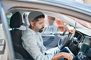 Young arab man sitting on car turning on radio at street