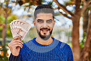 Young arab man smiling confident holding riyal banknotes at park