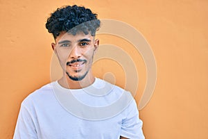 Young arab man smiling happy leaning on the wall at street of city