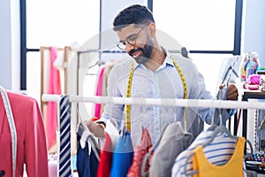 Young arab man tailor smiling confident holding clothes on rack at tailor shop