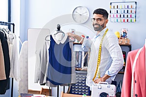 Young arab man tailor smiling confident holding t shirt at tailor shop