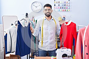 Young arab man tailor smiling confident holding t shirts at tailor shop