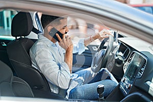 Young arab man talking on smartphone sitting on car at street