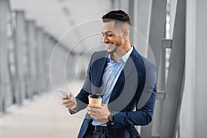 Young Arab Man Using Mobile Phone And Drinking Coffee In Airport