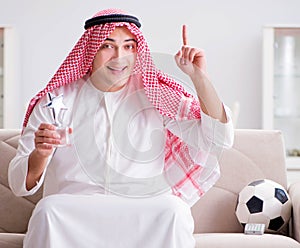 Young arab man watching football sitting on sofa