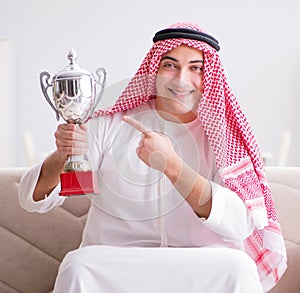 Young arab man watching football sitting on sofa