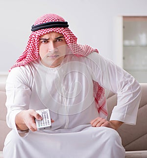 Young arab man watching tv sitting on the sofa