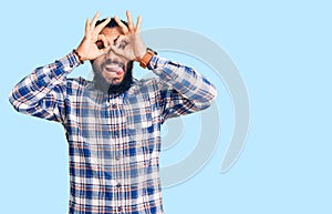 Young arab man wearing casual clothes doing ok gesture like binoculars sticking tongue out, eyes looking through fingers