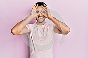 Young arab man wearing casual clothes doing ok gesture like binoculars sticking tongue out, eyes looking through fingers