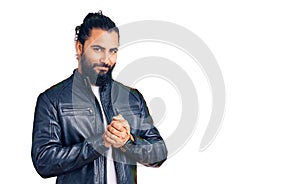 Young arab man wearing casual leather jacket with hands together and crossed fingers smiling relaxed and cheerful